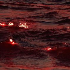 the sun is setting over the ocean with red lights in the water and some waves