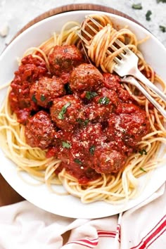 spaghetti and meatballs are served in a white bowl with a fork on the side