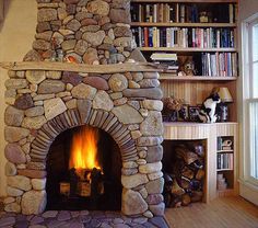 a stone fireplace in a living room next to a book shelf with books on it