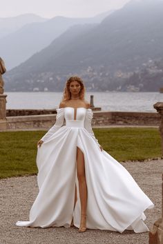 a woman in a white wedding dress posing for the camera with mountains in the background