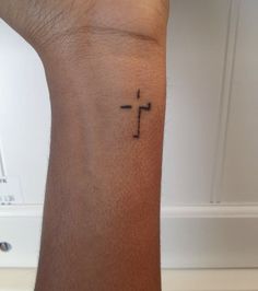 a small tattoo on the wrist of a person with a cross tattooed on their arm