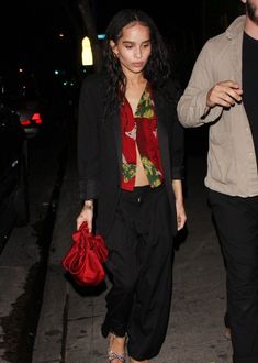 a woman in black pants and red scarf walking down the street with her handbag