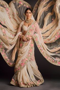 A stunning image of a Pakistani bride in an exquisite floral saree, with a delicate ivory base adorned with pastel pink and green embroidery. The saree is elegantly bordered with intricate gold zari work, adding a touch of opulence. The bride wears a low-cut blouse and is adorned with statement jewelry, including a magnificent necklace and earrings that enhance the grandeur of her bridal attire. The rich, layered drape of the saree flows effortlessly, creating a luxurious and modern bridal look that is truly captivating. Designer Sarees Wedding Party Wear, Net Saree Designs, Party Wear Sarees Online, Designer Sarees Wedding, Lehenga Saree Design, Trendy Outfits Indian, Wedding Party Wear, Sarees Wedding