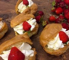 several pastries with cream and strawberries sitting on top of a wooden table next to some strawberries