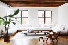 a living room with white couches and wooden floors in front of two large windows