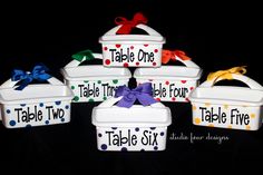 four white plastic containers with polka dot designs and bows on the lids are labeled table two, table three, table six