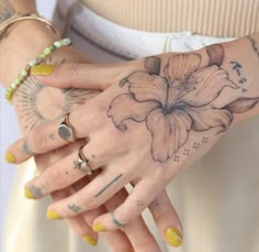 a woman's hands with tattoos and rings on her left hand, holding a flower