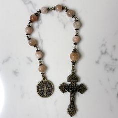 Handmade traditional Catholic single decade tenner rosary using Peach Moonstone smooth round stone beads. Antique bronze daisy bead caps on every bead with additional flower bead caps on Our Father bead. Antique bronze St. Benedict medal (Patron Saint of students) with Pardon Crucifix. Hail Mary beads are 8mm with the Our Father bead being 10mm. Designed to be used and/or displayed. Measures about 10.25" long. This rosary would make a beautiful gift for a baby shower, Baptism, First Communion, Reconciliation, Confirmation or any other special event or occasion. Comes in a beautiful black velvet pouch. I ship same or next business day. All of my rosaries are one of a kind and are my own personal creation. Photos are a part of the description-you will receive the exact rosary pictured. Pleas St Benedict Medal, Pocket Rosary, Benedict Medal, St Benedict, Our Father, Hail Mary, Peach Moonstone, Velvet Pouch, Patron Saints