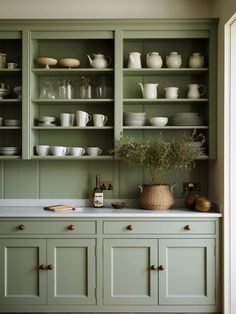 a kitchen with green cabinets and white dishes