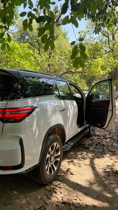 a white suv parked on the side of a dirt road with its door open and trees in the background