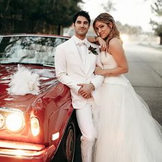 a bride and groom standing next to a red car