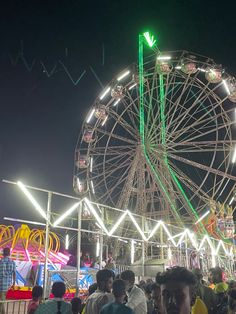 a large ferris wheel sitting next to a crowd of people at an amusement park in the night