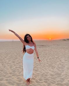 a woman standing on top of a sandy beach next to the sun in the sky