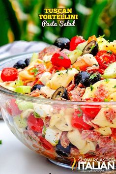 a salad with tomatoes, olives and other vegetables in a glass bowl on a table