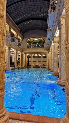 an indoor swimming pool in a hotel with columns and blue water running through the floor