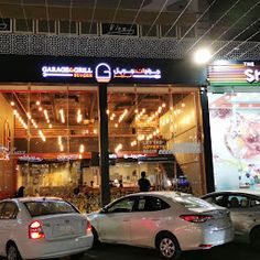 two cars parked in front of a restaurant with lights hanging from the ceiling above it