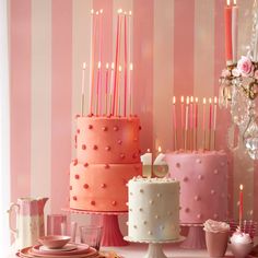 a table topped with three cakes covered in frosted icing and lit pink candles