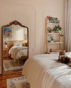 a cat laying on top of a bed next to a large mirror in a bedroom