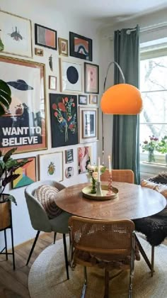 a dining room table with chairs and pictures on the wall behind it, surrounded by potted plants