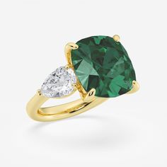 an emerald and diamond ring with two pear shaped diamonds on the side, set in yellow gold