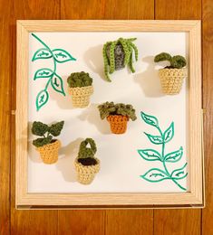 small crocheted potted plants are displayed in a shadow box on a wooden surface