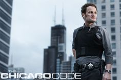 a man standing in front of tall buildings wearing a black shirt and police uniform with the chicago code written on it