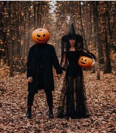 two people dressed up in halloween costumes holding hands and walking through the woods with pumpkins on their heads