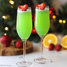 two wine glasses filled with green liquid and topped with strawberries on a table next to a christmas tree