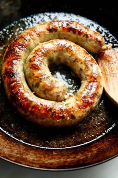 two sausages in a frying pan with a wooden spoon