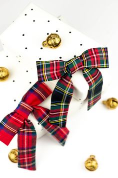 a red, green and blue plaid bow tie next to some gold bells on a white surface