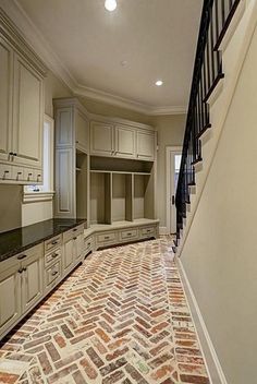 an empty kitchen with white cabinets and red brick flooring in the center, along with stairs leading up to the upper level