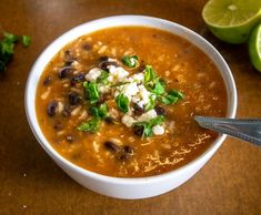 a close up of a bowl of soup on a table with limes and cilantro