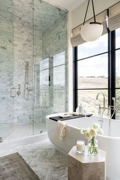 a white bathtub sitting next to a window in a bathroom with marble floors and walls