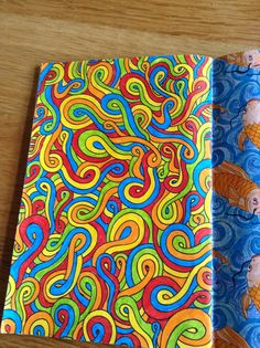 two colorful notebooks sitting on top of a wooden table