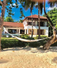 a hammock hanging between two palm trees in front of a large white house