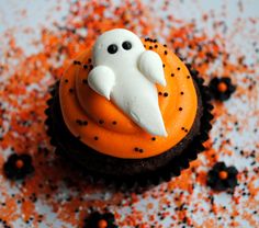 an orange cupcake with white frosting and black sprinkles on it