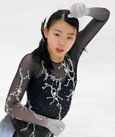 a young woman in a black dress skating on ice with her hands behind her head