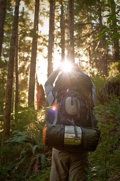 a man with a backpack walking through the woods in the sunbeams on a sunny day