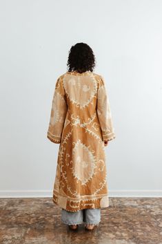 This semi-fitted duster was made from an antique hand-embroidered woven cotton Suzani, a textile traditionally used as wall hangings or in the yurts of nomadic people in Central Asia. An original aloka design, we prepared the vintage material with our signature multi-step shampoo and softening process. In our Athens, Georgia-based studio, our designers created this A-line semi fitted jacket with a plunging neckline and puffed bell sleeves. Served bound seams on the interior showcase the hand-stitching. Thick trim along the bottom of the jacket and sleeves give it a luxurious look and drape. Each textile bares memories and marks of the hand and past. Each piece is a one-of-a-kind garment. We carefully curate and prepare these beautifully preserved textiles and embrace imperfections, mending Traditional Brown Kimono For Festival, Traditional Beige Cotton Kimono, Traditional Brown Cotton Kaftan, Beige Embroidered Bohemian Kurta, Traditional Beige Kaftan For Festivals, Bohemian Beige Embroidered Kurta, Traditional Long Brown Kurta, Traditional Cotton Ikat Print Kimono, Traditional Cotton Kimono With Ikat Print