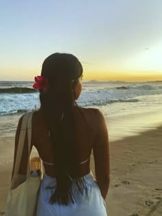 a woman standing on top of a sandy beach next to the ocean with her back to the camera