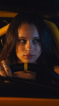 a woman sitting in the driver's seat of a car with her hand on the steering wheel