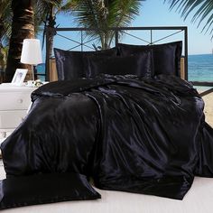 a bed with black sheets and pillows in front of palm trees on the beach,