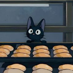 a black cat sitting on top of an oven filled with donuts