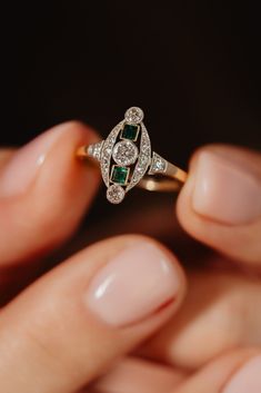 a close up of a person holding a diamond and emerald ring