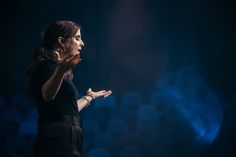 a woman standing in front of a crowd holding her hands out to the side while talking