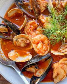 a bowl filled with seafood and mussels next to bread on a wooden table