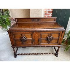 an old wooden chest with ornate carvings and knobs on the front, sitting next to a potted plant