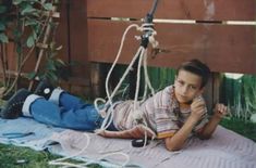 a young boy laying on top of a blanket talking on a cell phone next to a tree