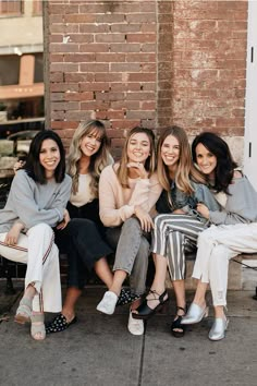 four women sitting on a bench in front of a brick wall and smiling at the camera