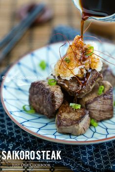 a plate with steak and mashed potatoes topped with scallions on it, sitting on a bamboo mat